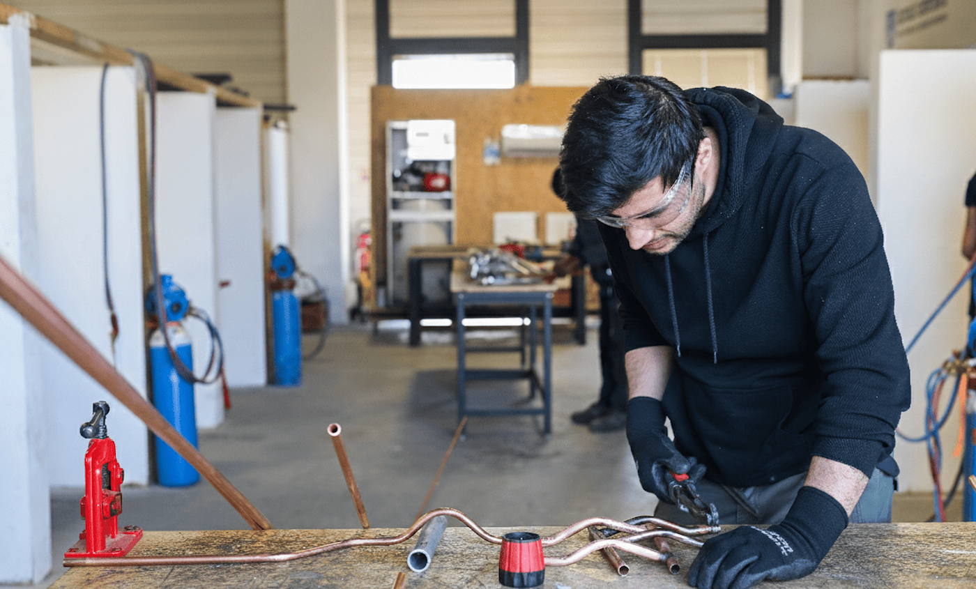 Apprenant en formation plomberie à l’École Gustave, travaillant des tuyaux en cuivre dans un atelier pédagogique.