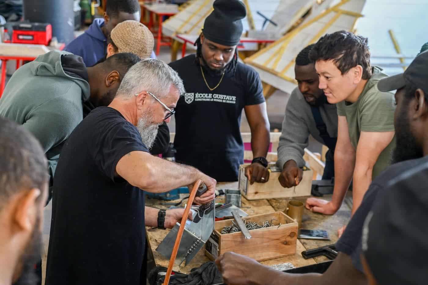 Groupe d’apprenants de l’École Gustave en atelier, autour d’un formateur qui démontre un geste professionnel de couverture-zinguerie.